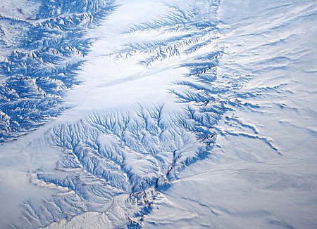 Luftaufnahme verschneite Landschaft mit tief eingeschnittenen, verzweigten Tälern