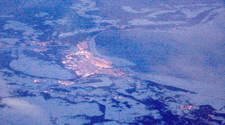 Stadt in verschneiter Ladnschaft an einem Gewässer in der Abenddämmerung, Luftaufnahme